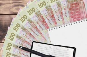 Ventilador de billetes de 100 hryvnias ucranianas y bloc de notas con libreta de contactos y bolígrafo negro. concepto de planificación financiera y estrategia empresarial foto