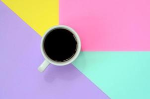 Small white coffee cup on texture background of fashion pastel blue, yellow, violet and pink colors paper in minimal concept photo