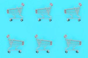 Shopping addiction, shopping lover or shopaholic concept. Many small empty shopping carts perform a pattern on a pastel colored paper background. Flat lay composition, top view photo