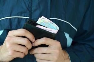 Man holds in hands black leather wallet with ukrainian money or thief who stole wallet full of money photo