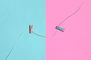 Two colored wooden pegs and small rope lie on texture background of fashion pastel blue and pink colors paper in minimal concept photo