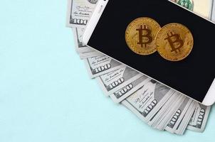 Bitcoins lies on a smartphone and hundred dollar bills on a light blue background photo