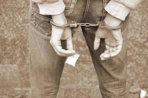 traficante de drogas arrestado esposado por la policía con un pequeño paquete de heroína en el fondo de la pared oscura foto