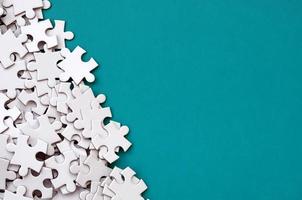 A pile of uncombed elements of a white jigsaw puzzle lies on the background of a blue surface. Texture photo with copy space for text
