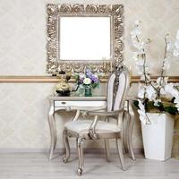 A fragment of a retro interior with a chair and table, on which is a telephone and a vase of flowers. Above the table hangs an empty picture frame for your photo