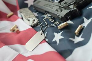 Army Dog tag token with 9mm bullets and pistol lie on folded United States flag photo