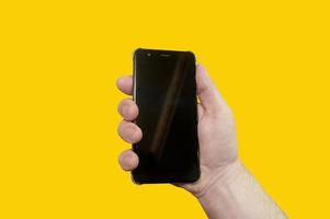 The hand with the phone isolated on a yellow background. photo