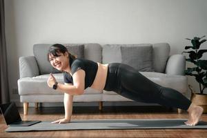 Asian chubby woman in living room practice online yoga lesson with the computer. female having meditate training class on the laptop. photo