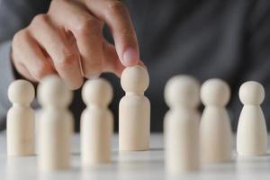 la mano del hombre elige una muñeca de clavija de madera. liderazgo y pensamiento creativo del equipo de negocios y recursos humanos para el trabajo en equipo o el concepto de jugador de equipo. foto