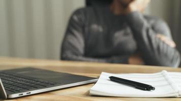 Tired businessman working on laptop with notepad and pen, resting head on hand, doing work overtime, stressed and bored photo