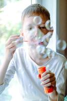 Boy blowing soap bubbles sitting on sofa at home. a lot of soap bubbles. Interesting games at home. magic bubbles photo