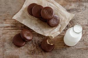 choco pie chocolate coated snacks and bottle of milk on wooden background, top view. Dessert with milk. Sweet snack. Brown colors photo