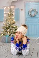 A smiling woman in a knitted sweater and a white hat lies on a terrace decorated for the Christmas holidays. Portrait of a cute girl on a bright veranda in Christmas clothes photo