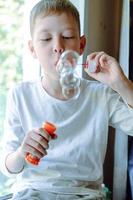 Boy blowing soap bubbles sitting on sofa at home. a lot of soap bubbles. Interesting games at home. magic bubbles photo