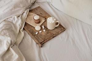 coffee with marshmallows and macaroons on a wooden tray, in bed. Aesthetically beautiful frame. Desserts in bed. hot chocolate with marshmallows. Cozy and warm day in bed photo