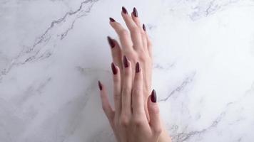 hermosas manos de una mujer joven con manicura roja oscura en las uñas.
