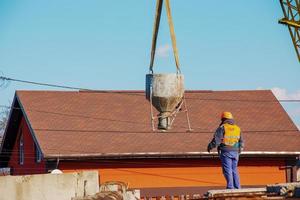 Construction of a bypass road in the industrial area. Builder worker takes the load with concrete from the boom of the crane photo