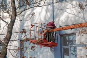 Builder in a crane basket repairs the coating of a metal structure on the wall of the facade of a building photo