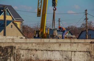 Dnepropetrovsk, Ukraine - 02.21.2022 Construction of a bypass road in the industrial area. Builder worker takes the load with concrete from the boom of the crane. photo