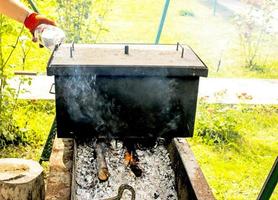 Smokehouse for hot smoking on fire. A man pours water into the shutter of a smokehouse photo