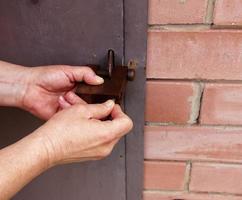 Women's hands open a rusty lock with keys. Lock on a metal door. Security. photo