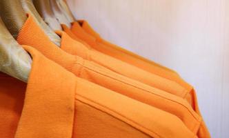 Many orange color shirts hanging on a rack photo