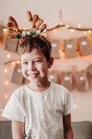 Happy boy greets Christmas. Christmas mood at home. Boy rejoices at Christmas. Christmas morning. A boy with deer antlers greets Christmas. photo