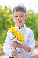 a cute boy in a field of sunflowers in a white shirt stands and smiles. photo