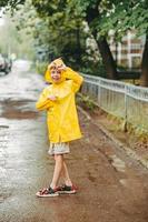 cute boy in a yellow raincoat and sandals is having fun, running through the puddles, in the city. jump through muddy puddles. Happy and carefree childhood photo