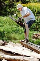 a man in shorts and a panama saws a tree with a chainsaw in his hands photo