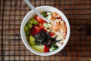 poke de aguacate, arroz, pepino, tomate y salmón sobre un fondo de madera. espacio de copia de plato asiático foto