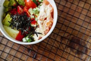 avocado, rice, cucumber, tomato and salmon poke on a wooden background. Asian dish copy space photo