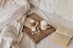 coffee with marshmallows and macaroons on a wooden tray, in bed. Aesthetically beautiful frame. Desserts in bed. hot chocolate with marshmallows. Cozy and warm day in bed photo