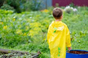 A boy in a yellow raincoat walks in the rain, back view. A child on the street. Bright clothes. Walk in the rain. photo