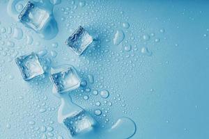 Ice cubes with drops of melt water water on a blue background, top view. photo