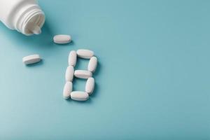 White capsules with vitamins in the form of B poured from a jar on a blue background photo