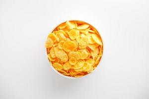 White cup with golden corn flakes isolated on white background. View from above. Delicious and healthy breakfast photo