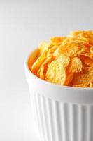 White cup with golden corn flakes isolated on white background. View from above. Delicious and healthy breakfast photo