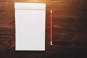 Notebook with a red pencil on a brown background with warm sunlight, for writing. Free empty space for writing on a blank sheet of a notebook. photo