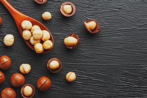 Shelled macadamia nut and peeled macadamia nut on a black textural background in a wooden spoon. Low contrast photo