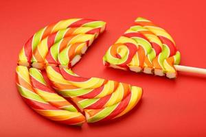 A large multi-colored Lollipop split into pieces, on a scarlet background. photo