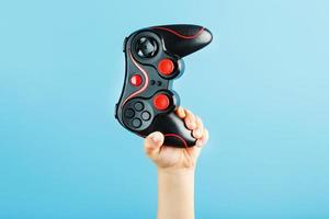 A child's hand triumphantly holds the gamepad on a blue background. Clear space photo