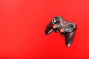 A black joystick game controller hovers isolated on a red background. Interactive entertainment photo