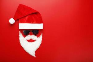 Santa Claus Hat and beard made of snow with black glasses on red background. photo