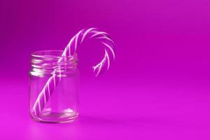 un bastón de caramelo de piruleta en un frasco de vidrio sobre un fondo rosa. foto