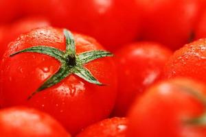 Lots of fresh ripe tomatoes with drops of dew. Close-up background with texture of red hearts with green tails. Fresh cherry tomatoes with green leaves. Background red tomatoes photo