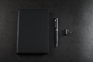 Black Notepad with a black pen on a black background. photo