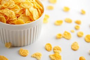 White cup with golden corn flakes, isolated on white background. Hopya crumbled around the cup. View from above photo