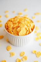 White cup with golden corn flakes, isolated on white background. Hopya crumbled around the cup. View from above. Delicious and healthy breakfast photo