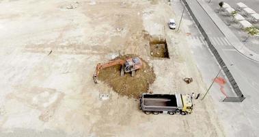 An Empty Truck Moving Near An Excavator At The Construction Site - aerial drone video